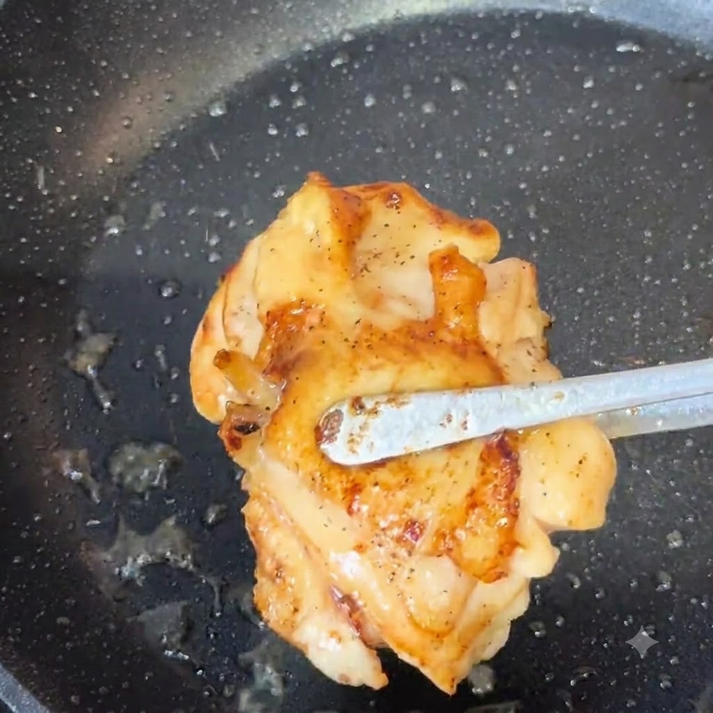 Unas pinzas levantando un muslo de pollo cocido y dorado de una sartén.