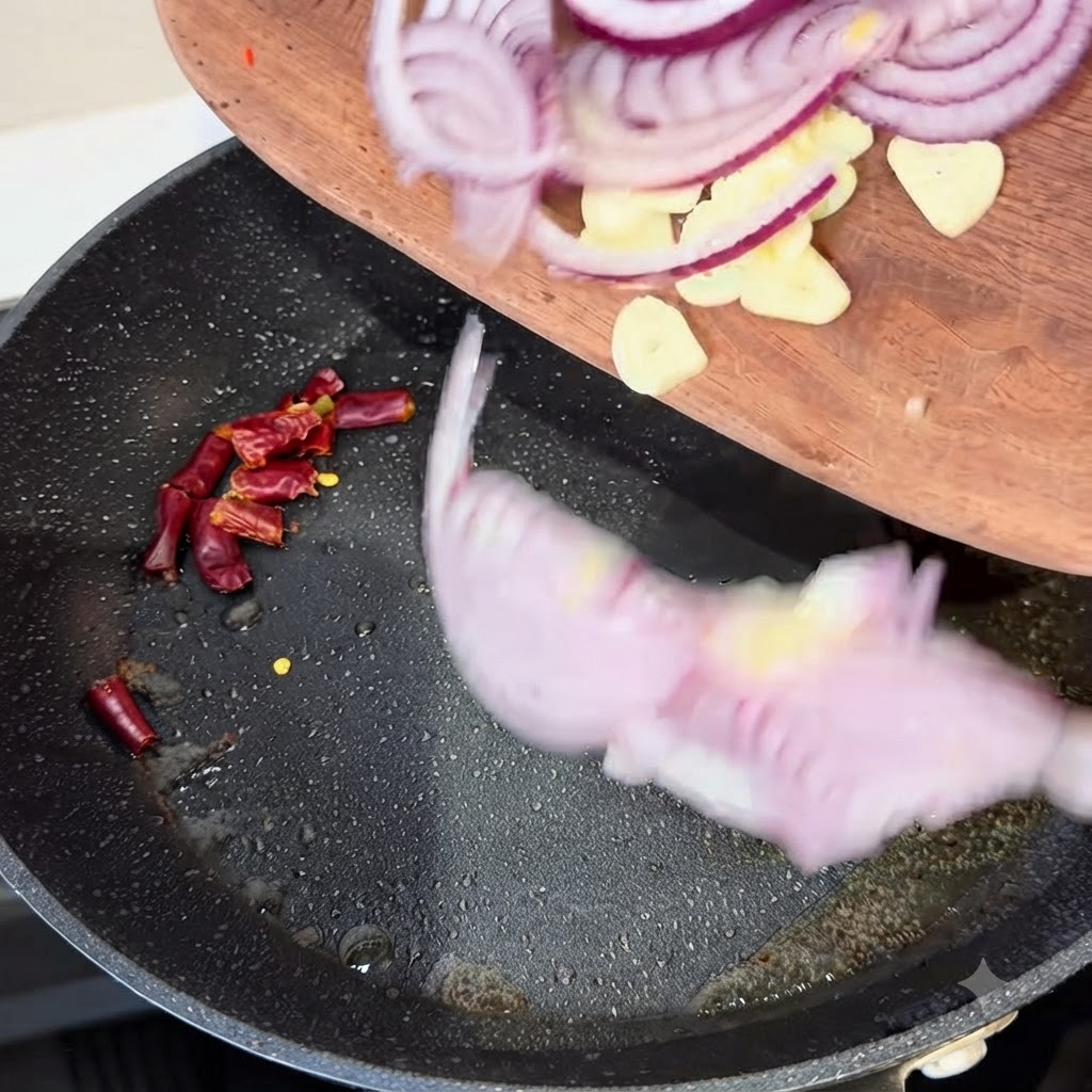 Tiras de cebolla roja, dientes de ajo y chiles secos siendo transferidos desde una tabla de madera a una sartén caliente.