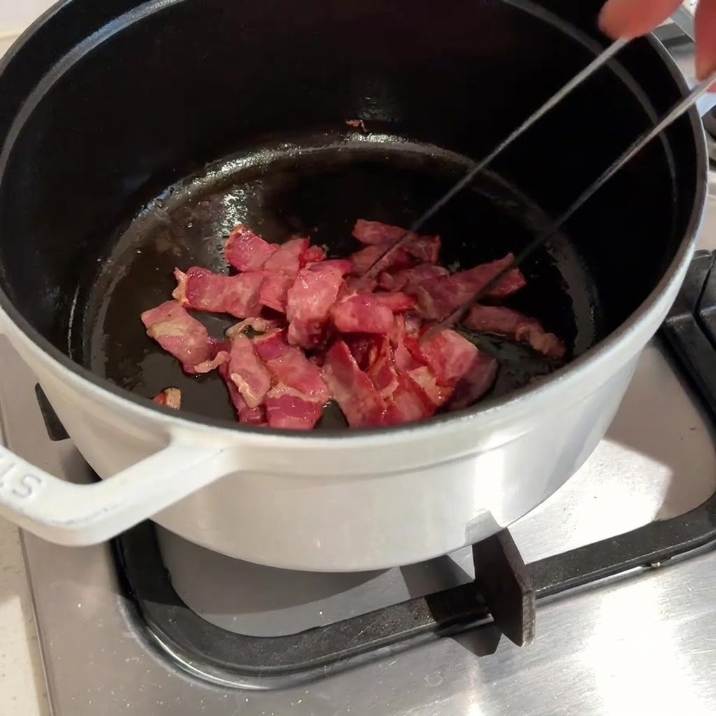 Tocino picado siendo salteado y frito en una olla oscura usando pinzas de metal.