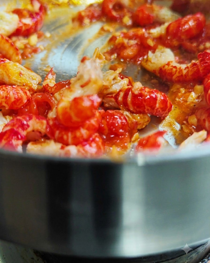 Colas de cangrejo peladas siendo removidas y salteadas en una sartén caliente con salsa de tomate roja.