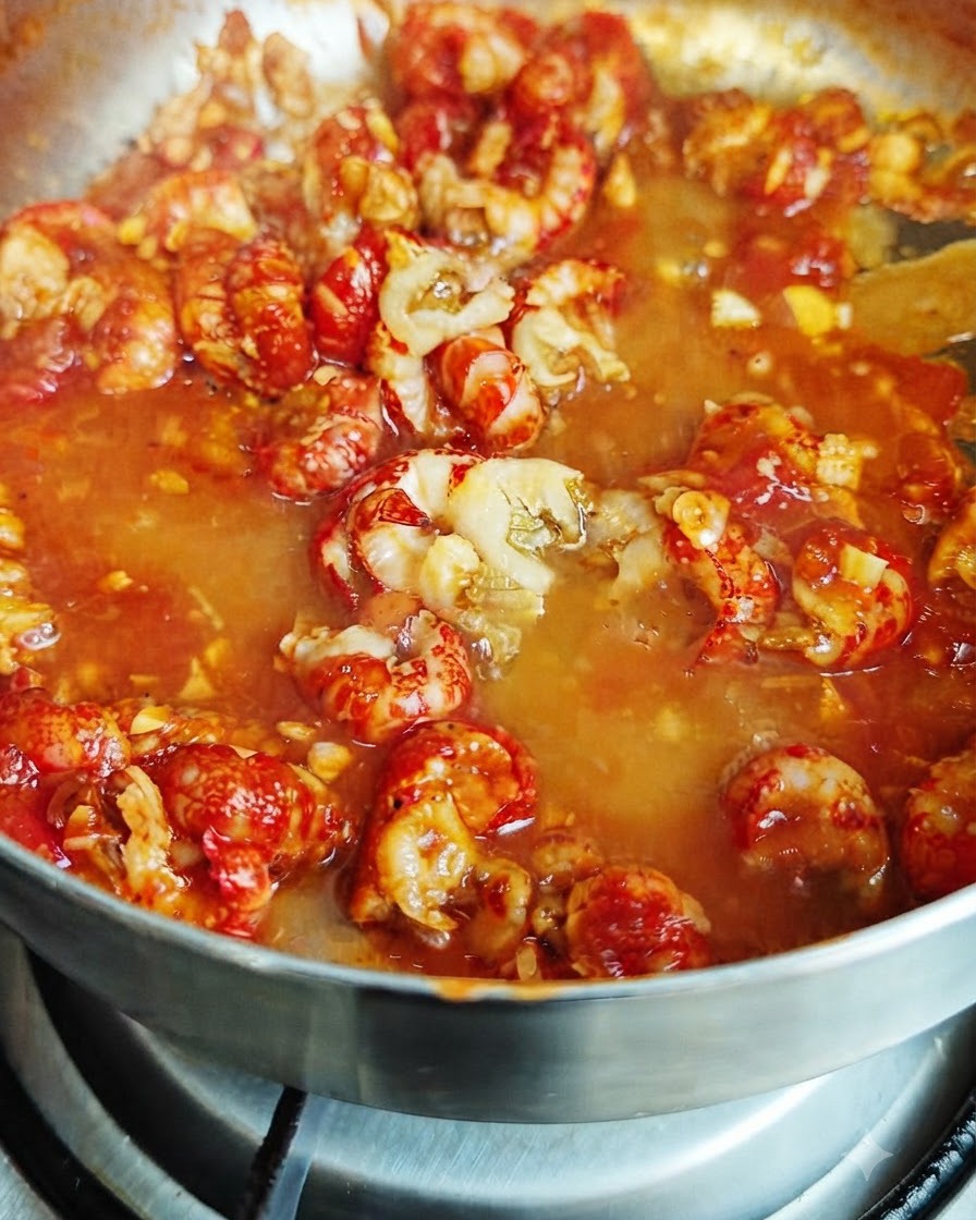 Leche siendo vertida en la mezcla de salsa roja burbujeante que contiene colas de cangrejo de río.