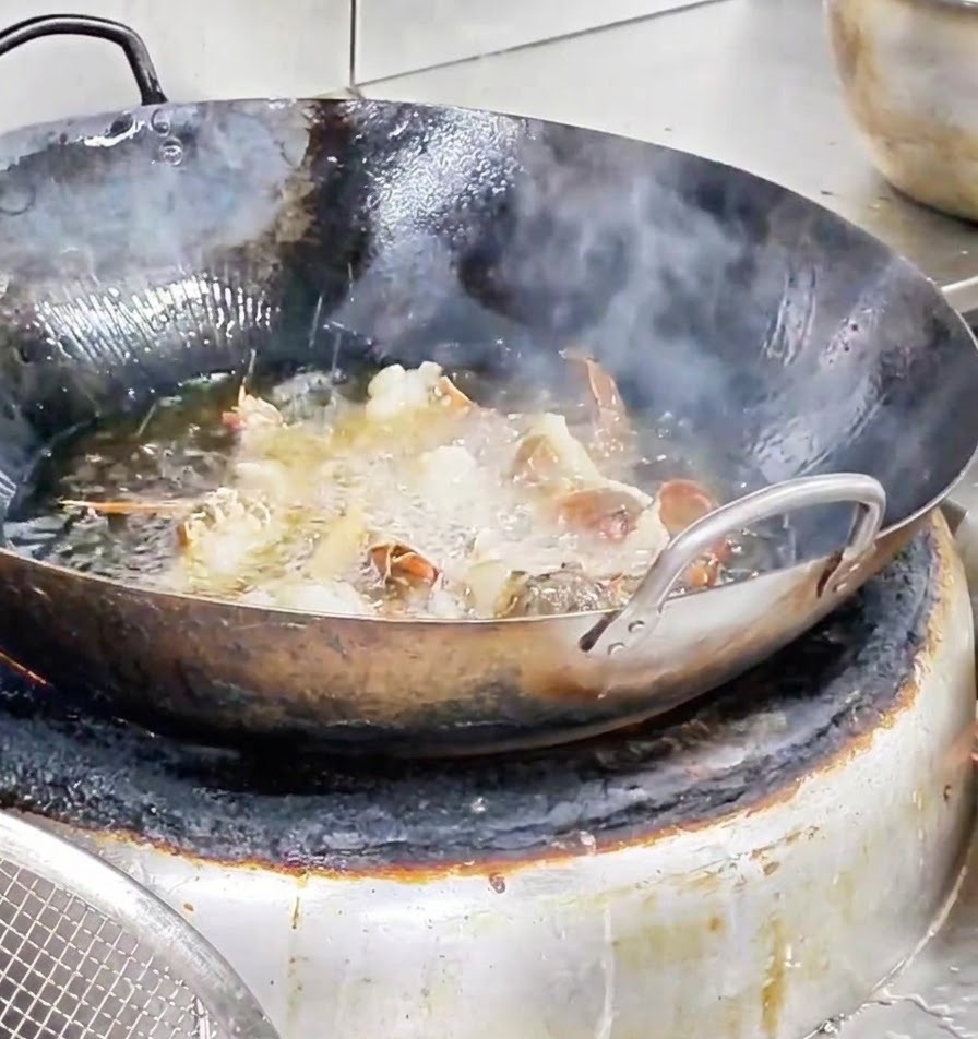 Trozos de langosta friéndose vigorosamente en un wok lleno de aceite caliente burbujeante.