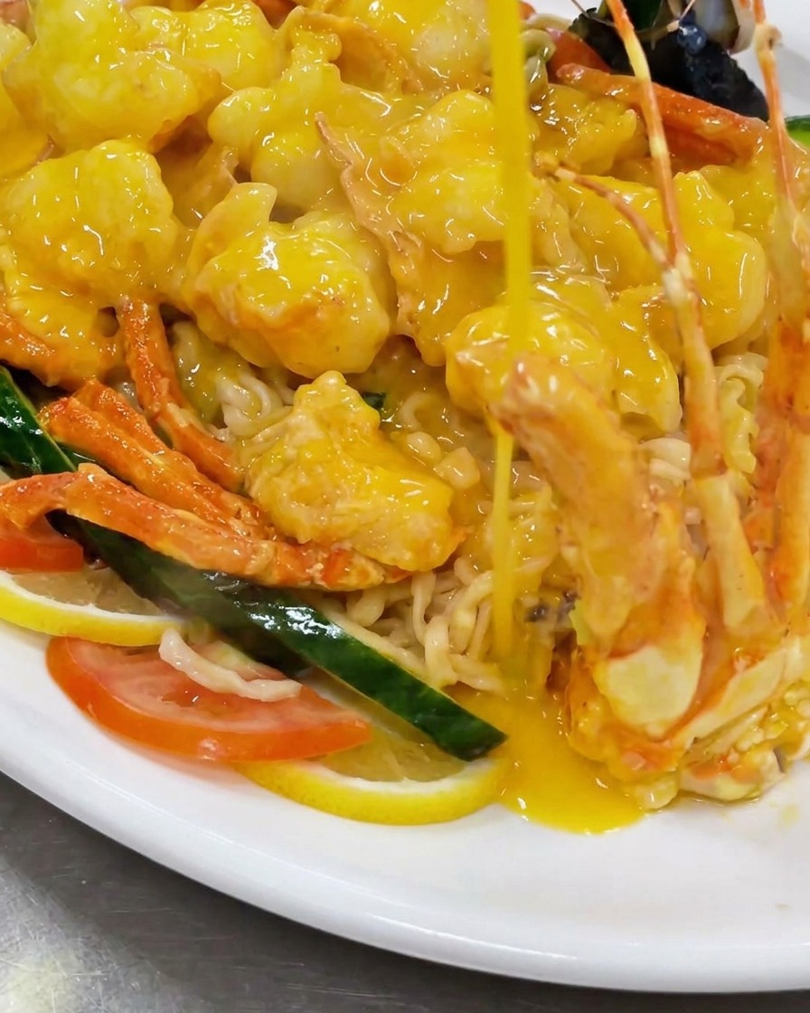 Vertiendo trozos de langosta frita en un wok lleno de una rica salsa de queso amarillo burbujeante.