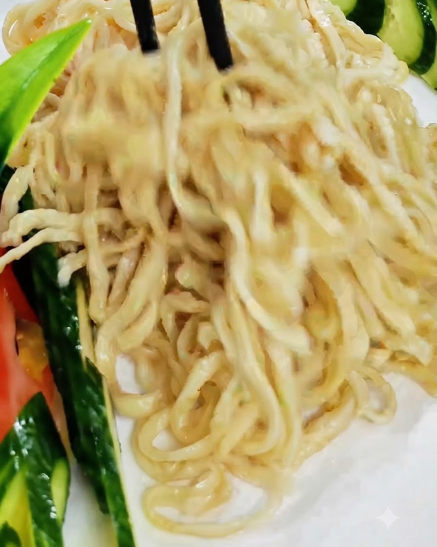 Palillos negros levantando y organizando fideos cocidos en un plato blanco adornado con pepino.