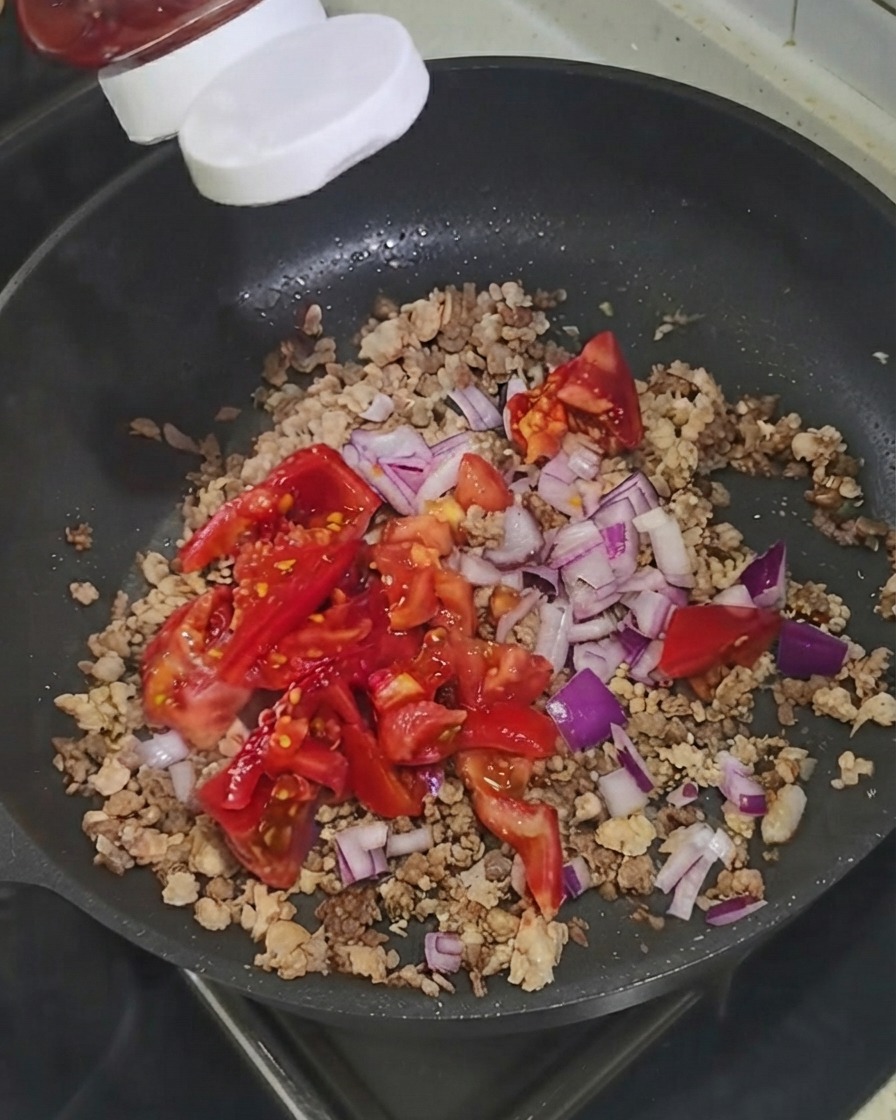 Kétchup siendo exprimido desde una botella directamente sobre los ingredientes en la sartén.