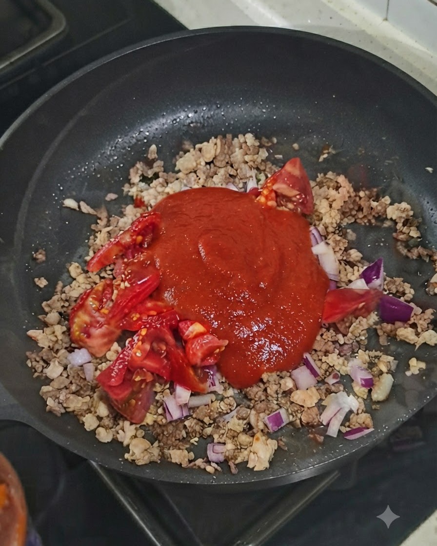 Una cucharada de pasta de tomate colocada sobre la mezcla de carne y verduras en la sartén.