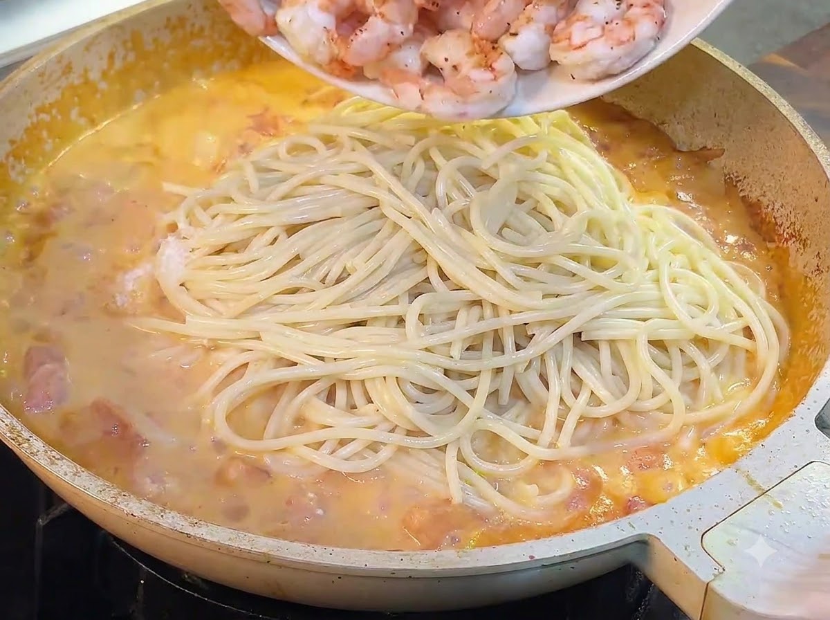 Camarones cocidos siendo vertidos desde un plato a la sartén con espaguetis y salsa.