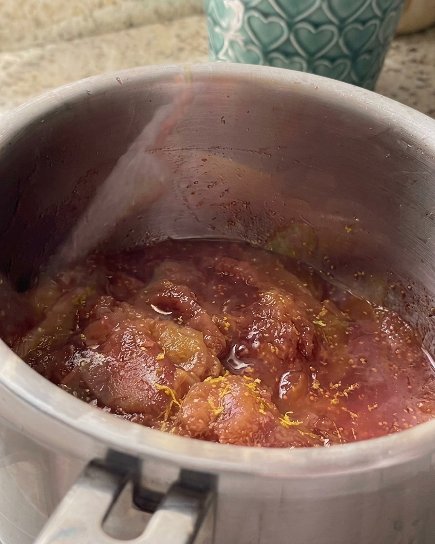 Ralladura y zumo de limón mezclándose con la salsa de higos a fuego lento en un cazo de acero inoxidable.
