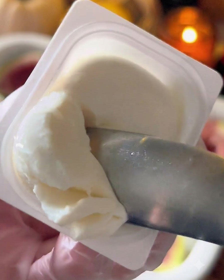 Un cuchillo pequeño o una cuchara tomando queso labneh blanco de un recipiente.