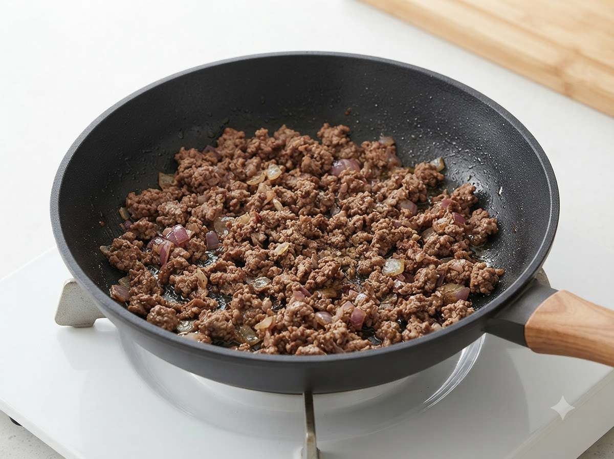 Carne picada cocida y cebollas mezcladas dentro de una sartén.
