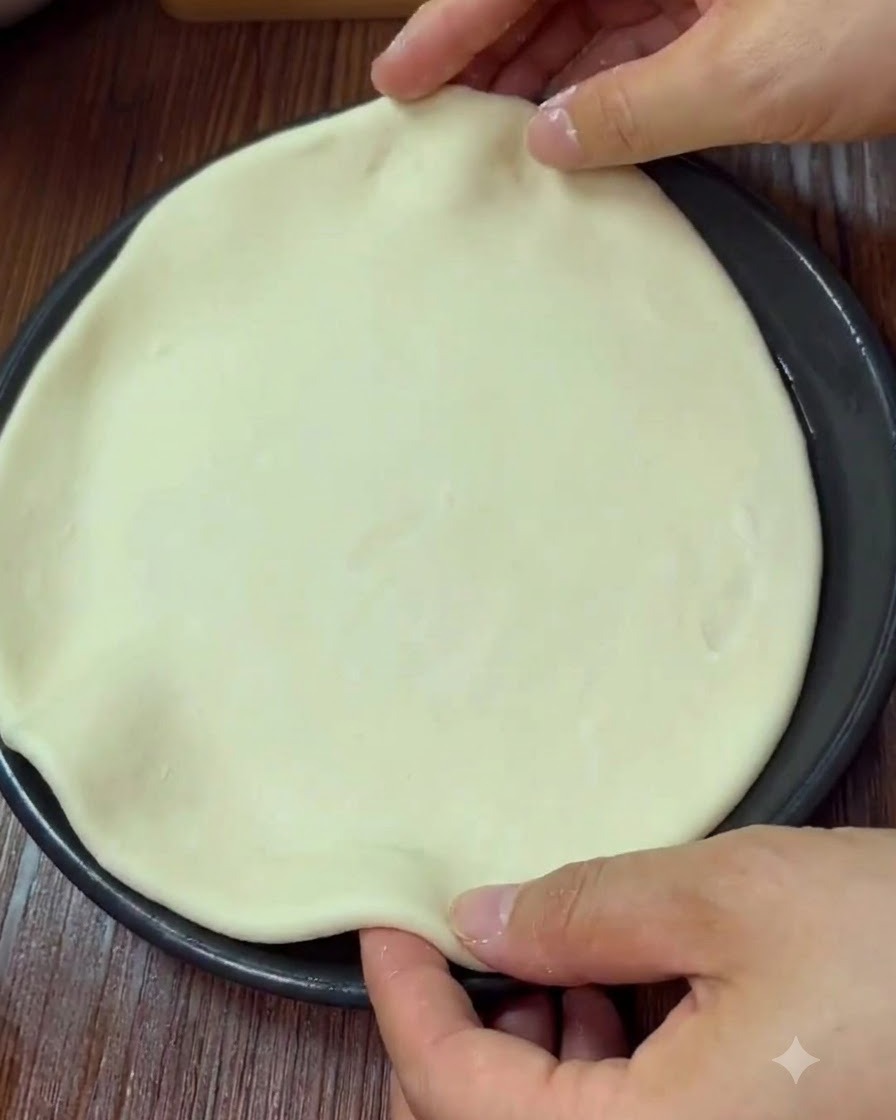 Manos dando forma y pellizcando el borde de una masa de pizza redonda dentro de una bandeja de horno.