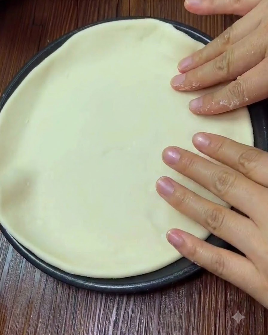 Manos presionando suavemente sobre la superficie de una masa de pizza aplanada.
