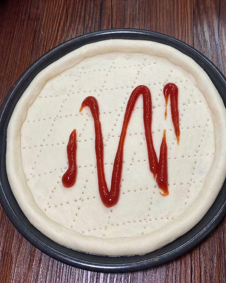 Queso mozzarella rallado esparciéndose uniformemente sobre la salsa de tomate en la masa de pizza.