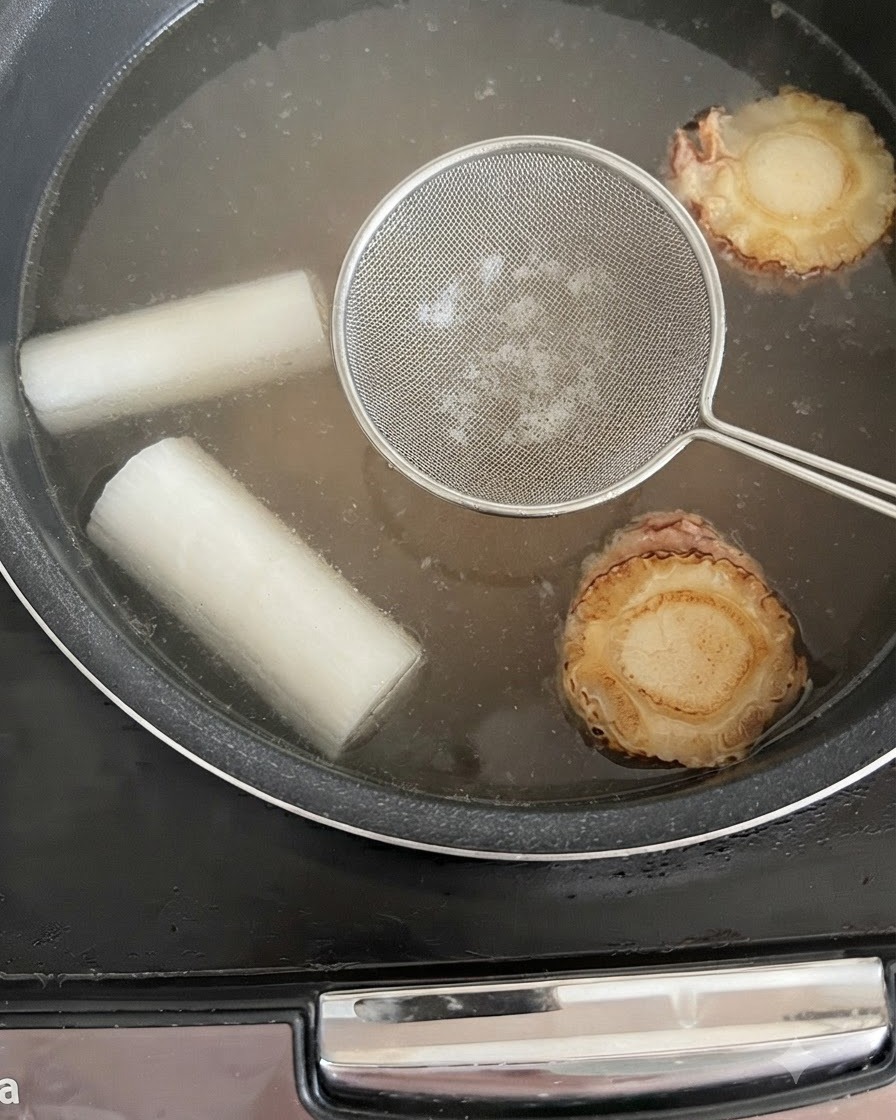 Una espumadera colocada sobre el caldo a fuego lento en la arrocera para eliminar impurezas.