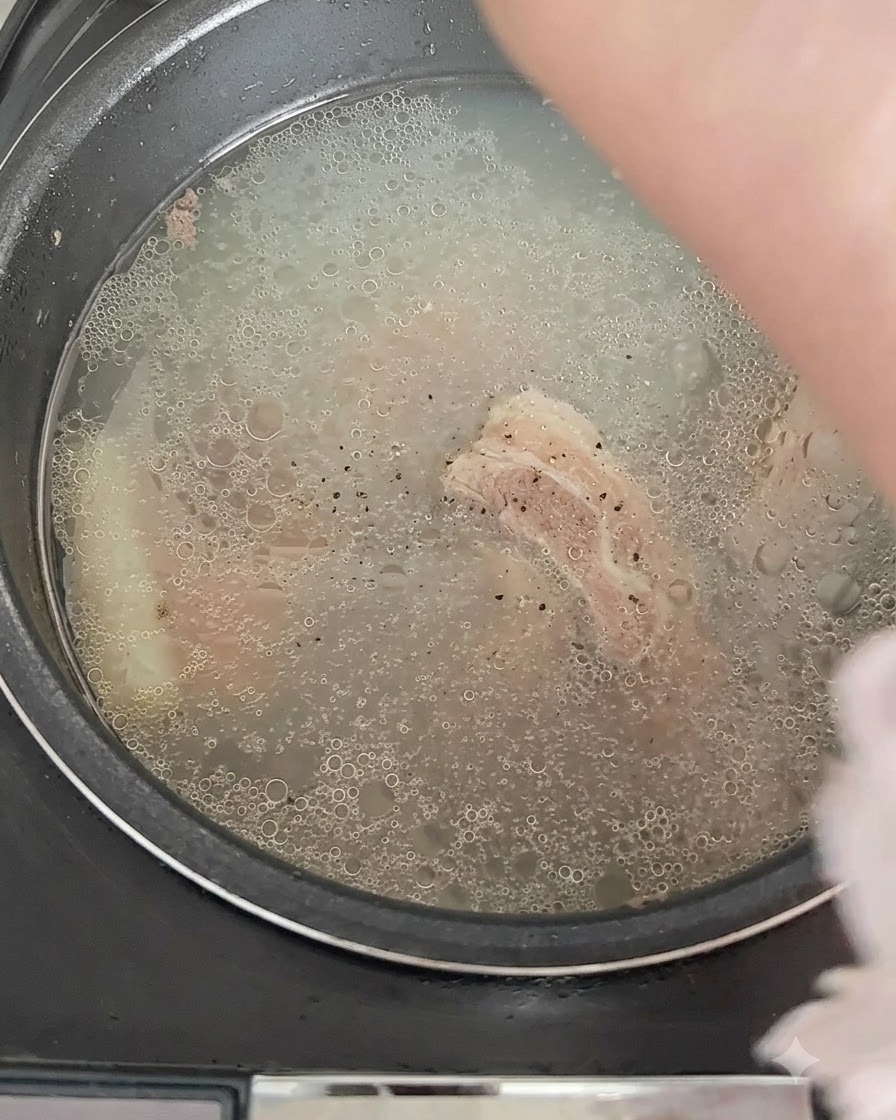Pimienta negra siendo espolvoreada sobre el caldo burbujeante en la arrocera.