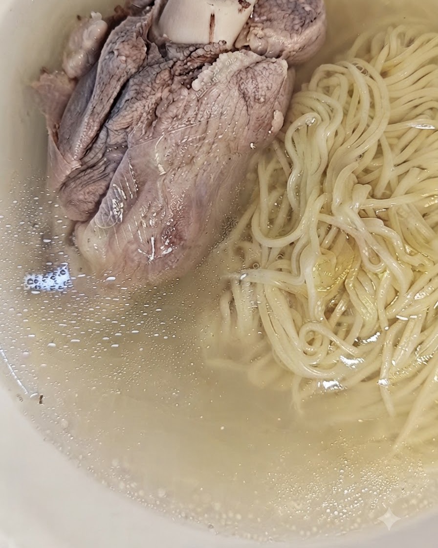 Un gran hueso de cerdo cocido colocado encima de los fideos y el caldo en un tazón, listo para servir.