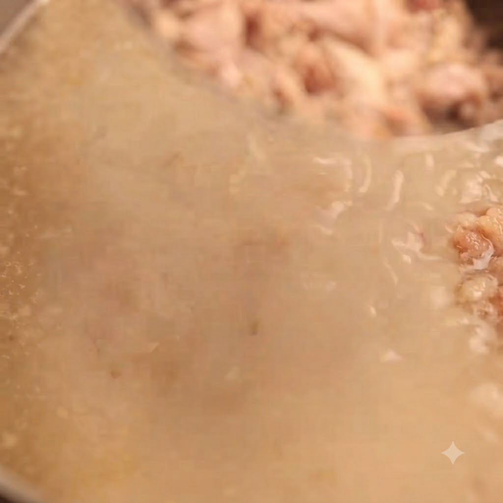 Caldo de hueso de cerdo blanco lechoso colándose a través de un colador de malla fina para atrapar los trozos de carne restantes.