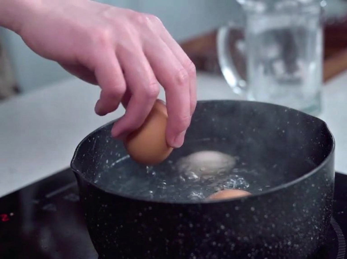 Huevos colocados suavemente en una olla de agua hirviendo y burbujeante usando una mano.