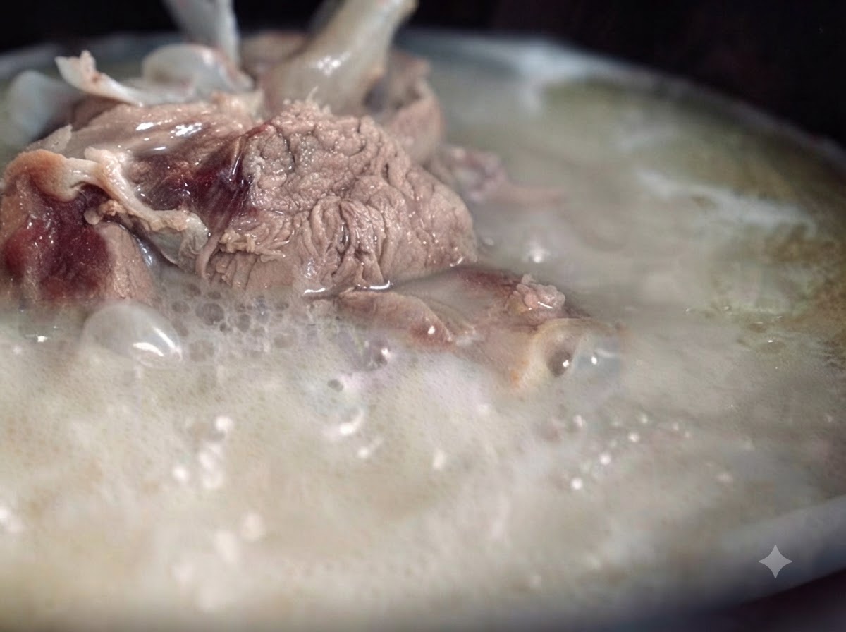 Un caldo de huesos de cerdo espeso, lechoso y opaco hirviendo vigorosamente en una olla, con trozos de carne y hueso visibles.