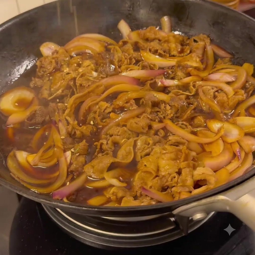 Ternera y cebollas cociéndose a fuego lento en una salsa teriyaki oscura y sabrosa dentro de una sartén.