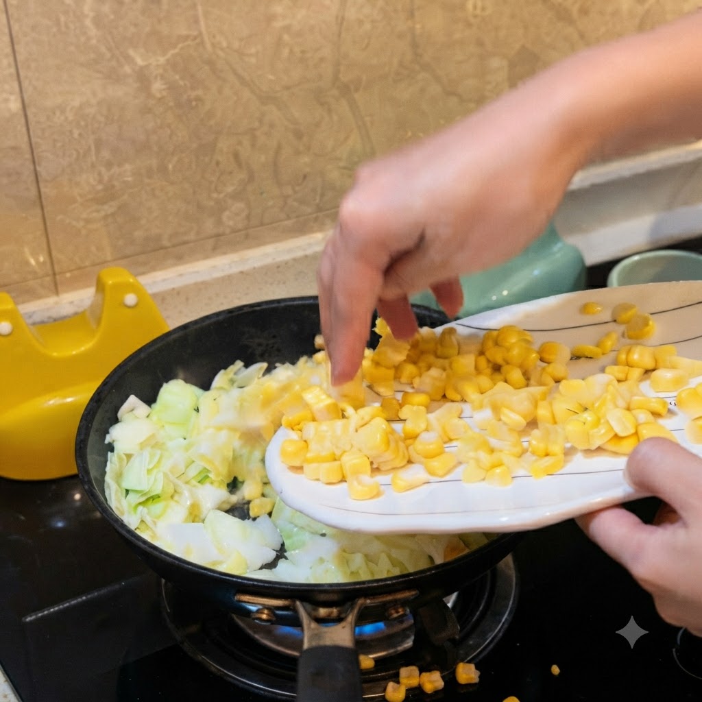 Una mano vertiendo granos de maíz amarillo desde un plato blanco hacia una sartén con col picada.