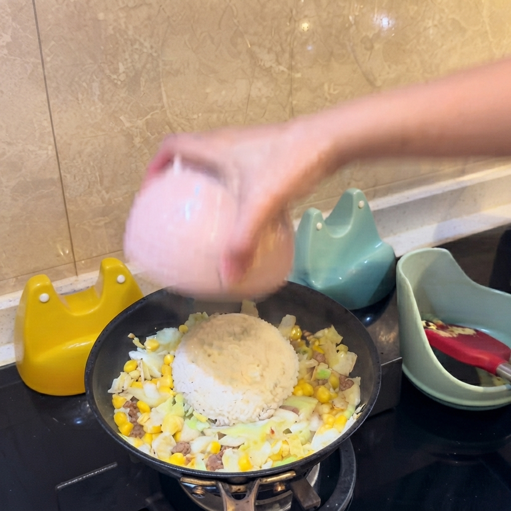 Un tazón rosado volcando un montículo de arroz blanco directamente hacia el centro de los ingredientes de la sartén.