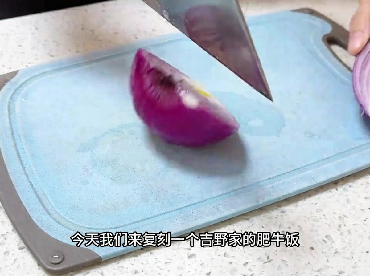 Un cuchillo de cocina cortando una cebolla morada en trozos finos sobre una tabla de cortar azul.