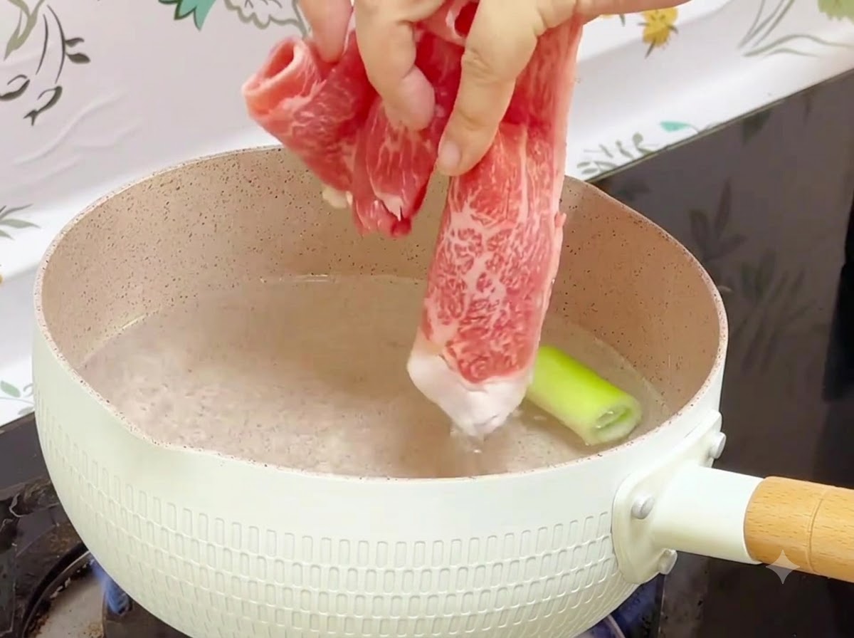 Rollitos de ternera congelados siendo añadidos a una olla con agua hirviendo y una pieza de cebollín dentro.