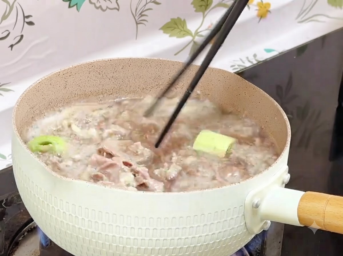 Palillos sacando rollitos de ternera blanqueados de una olla hirviendo hacia un recipiente.