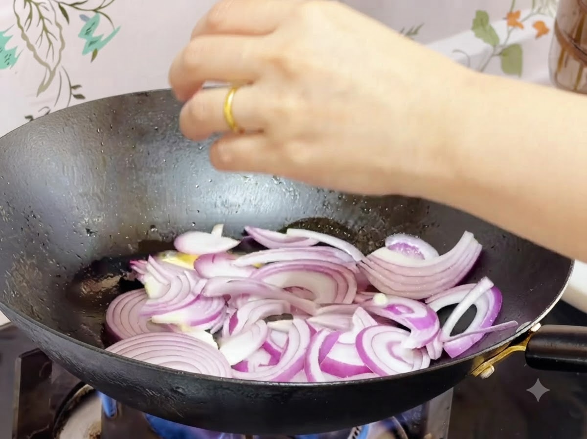 Cebollas moradas cortadas salteándose en mantequilla derretida dentro de un wok.