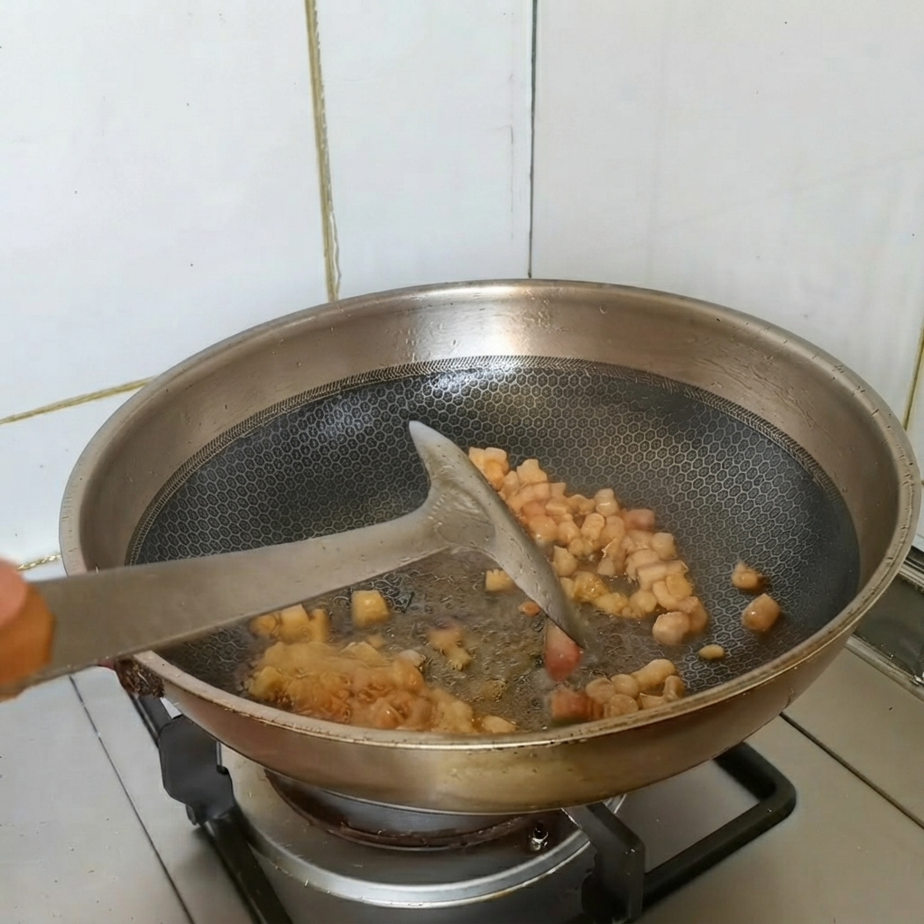 Trozos de panceta de cerdo dorándose mientras se saltean en un wok con ingredientes aromáticos.