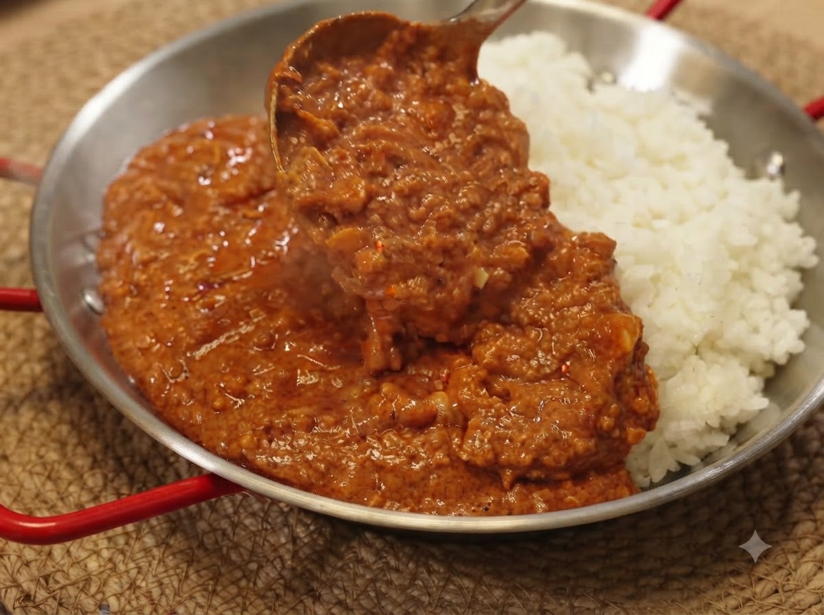 Un cucharón sirviendo rica salsa de cerdo picado al curry sobre una cama de arroz blanco en una sartén de servicio.