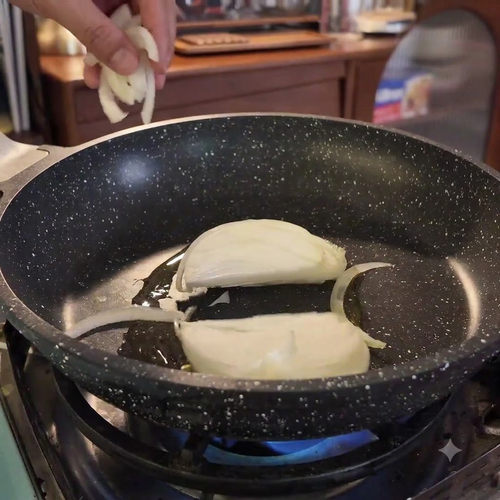 Rodajas de cebolla siendo añadidas a una sartén caliente con aceite sobre una llama azul.