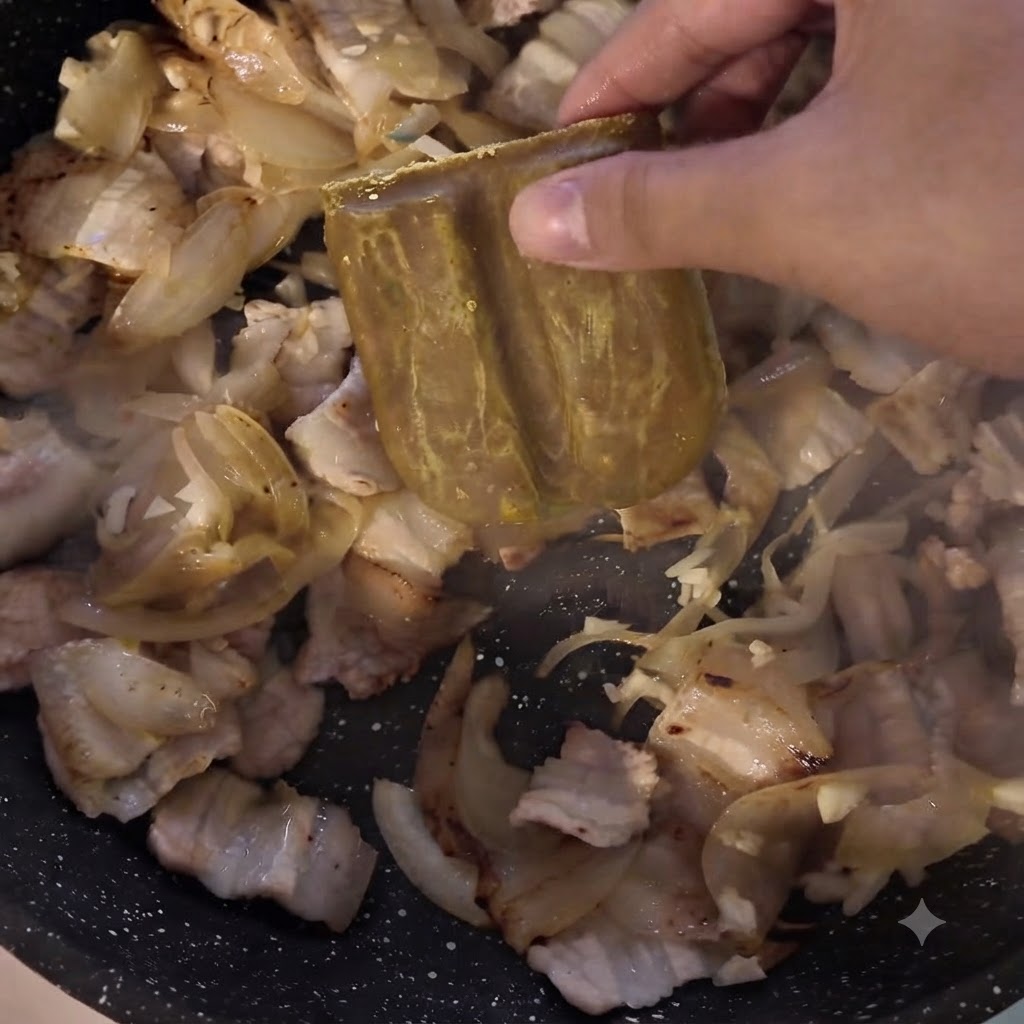 Un bloque de pasta de curry siendo añadido a la sartén que contiene carne y cebollas.