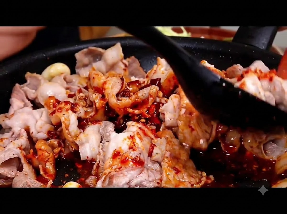 Una espátula negra mezclando la salsa roja picante con las rodajas de cerdo en una sartén caliente.