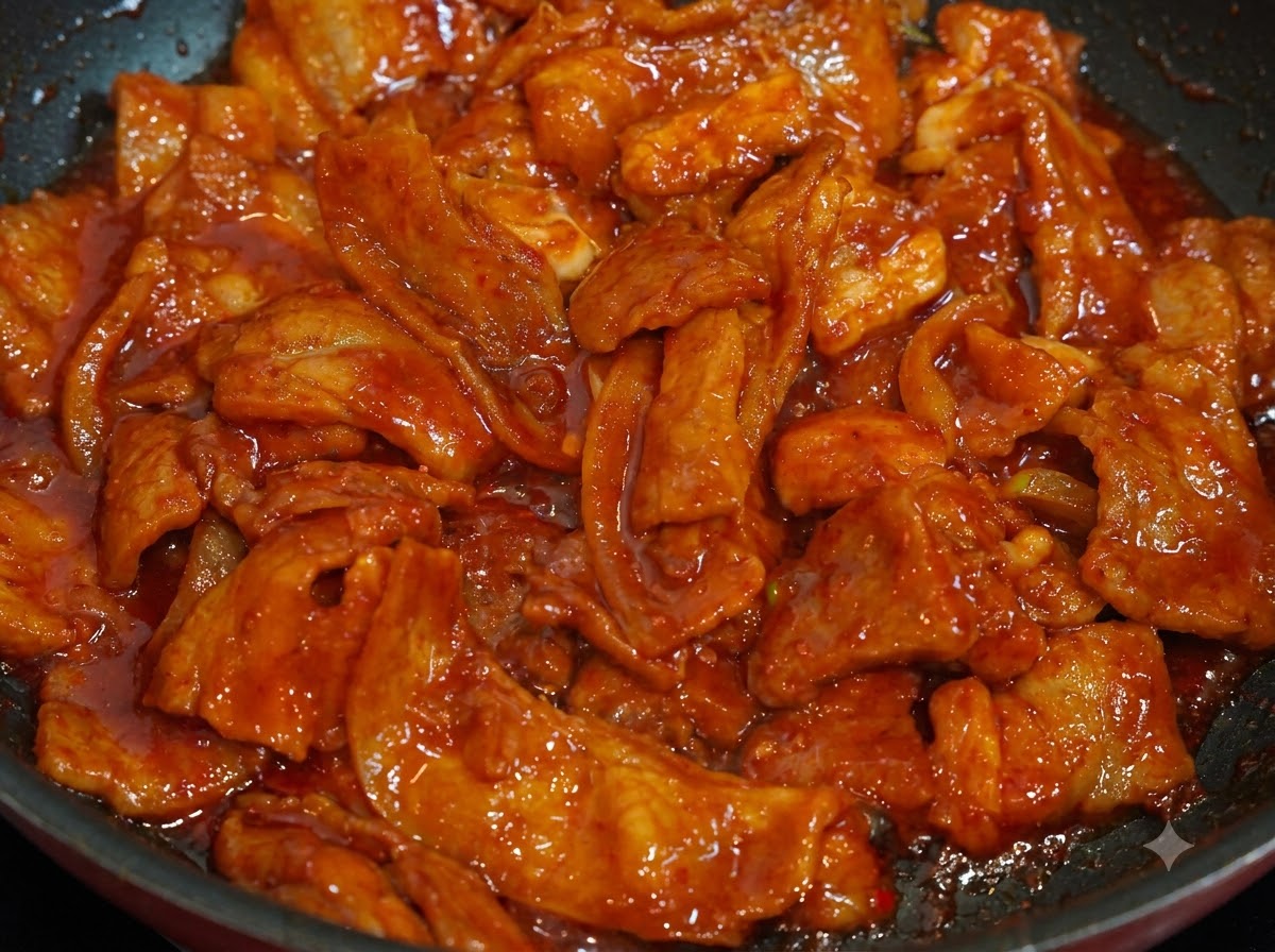 Primer plano de cerdo picante cocido en una sartén espolvoreado con semillas de sésamo blanco.