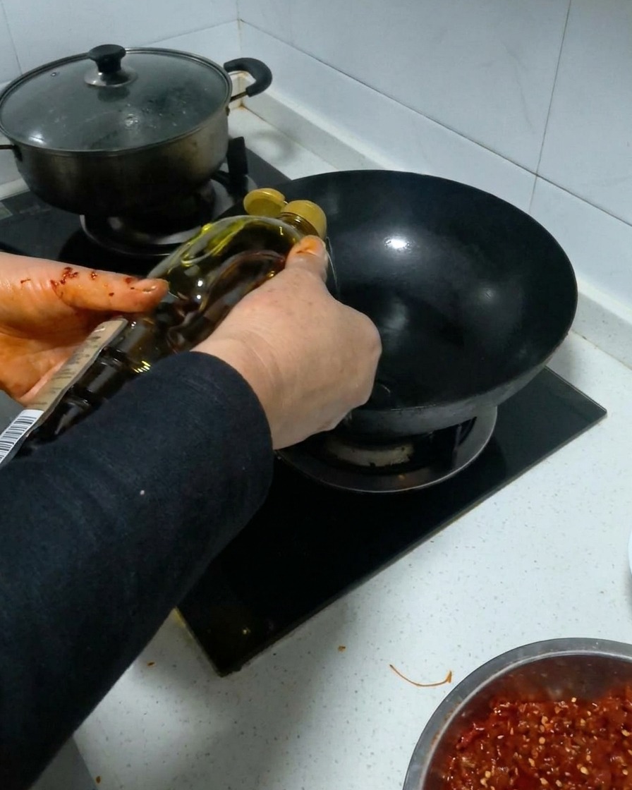 Aceite de cocina siendo vertido desde una botella en un wok negro caliente.