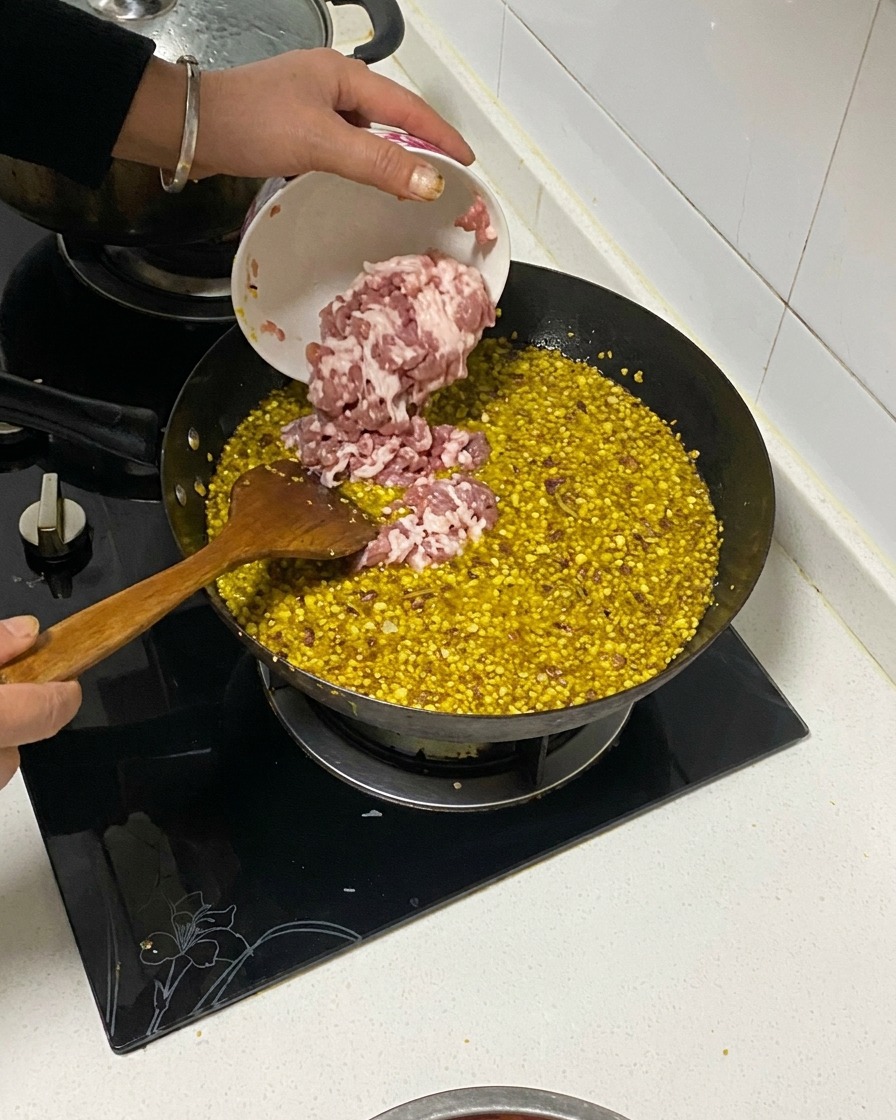Panceta de cerdo en cubos siendo vertida desde un pequeño tazón hacia un wok que contiene aromáticos fritos y aceite.