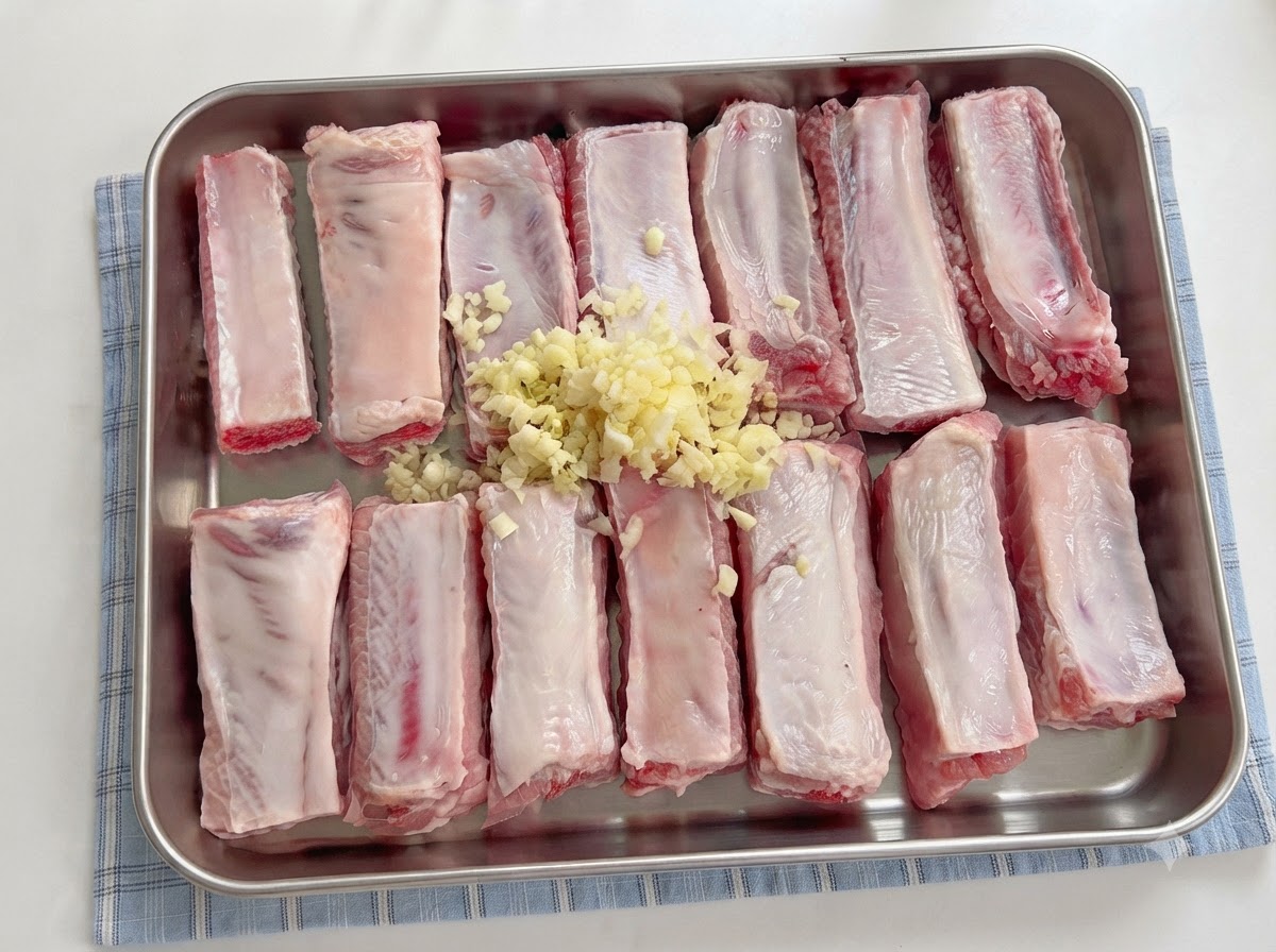 Salsas siendo vertidas desde una cuchara sobre las costillas sazonadas con ajo picado.