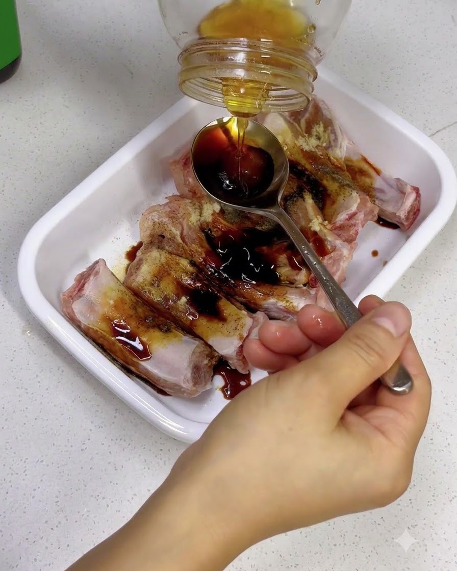 Mano sosteniendo una cuchara para atrapar miel dorada que se vierte desde un frasco de vidrio sobre costillas sazonadas.