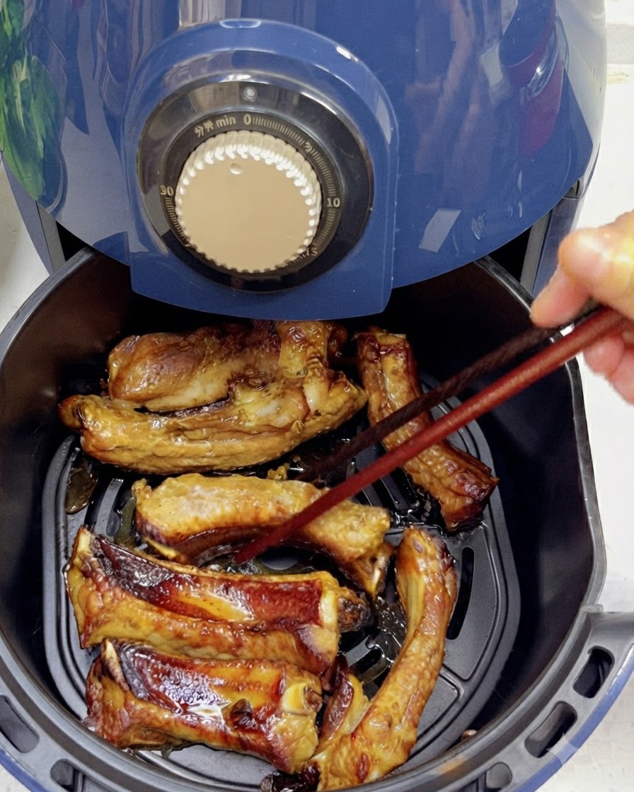 Usando palillos para voltear costillas de cerdo parcialmente cocidas y doradas dentro de una canasta de freidora de aire.