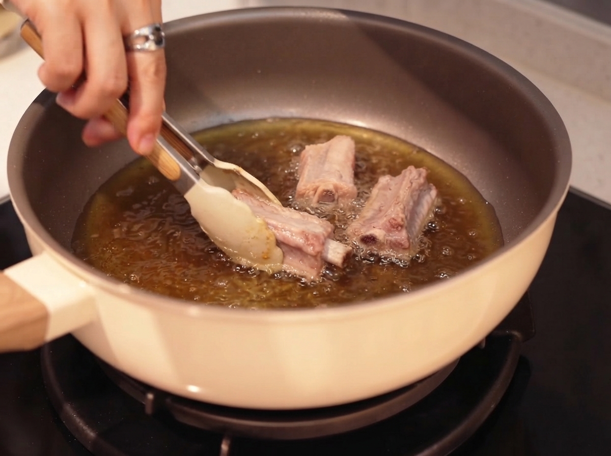 Costillas de cerdo friéndose en aceite caliente usando pinzas.