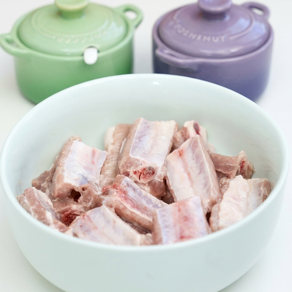 Costillas de cerdo crudas en un bol blanco siendo sazonadas con ajo, salsas de soya, salsa de ostras y especias.