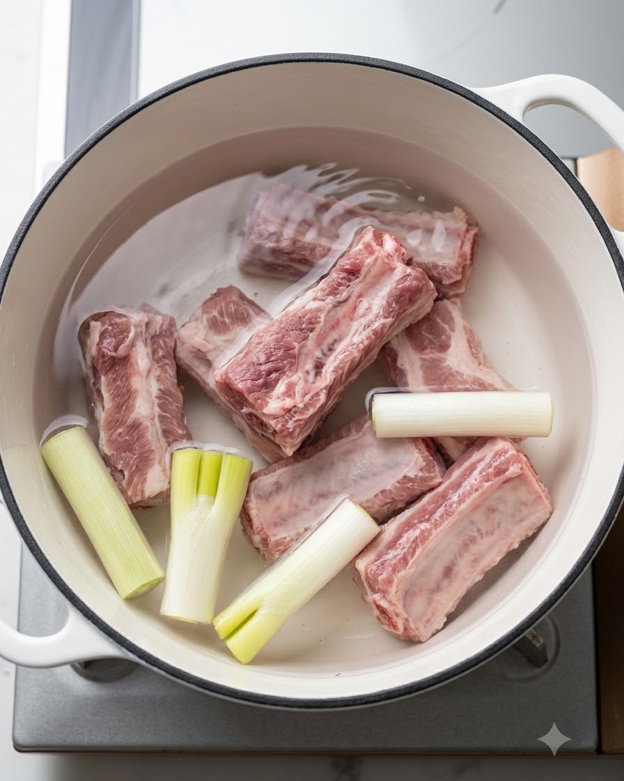Costillas de cerdo frescas en una olla con agua fría, cebollas verdes y aromáticos antes de hervir.