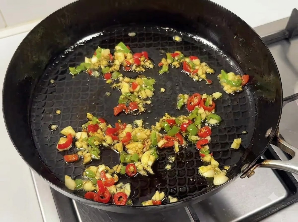 Una sartén con ajo y chiles salteados mezclados con una salsa oscura y sabrosa.
