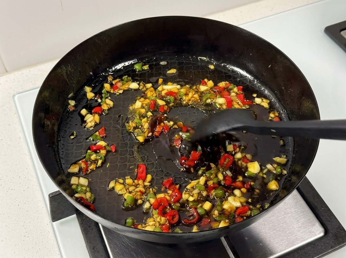 Una espátula removiendo costillas de cerdo y salsa dentro de una sartén en el fuego.