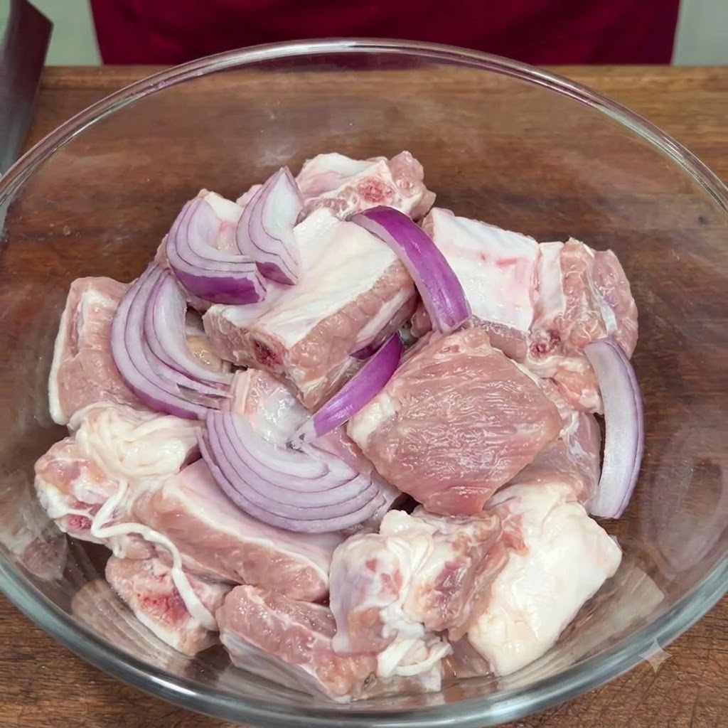 Cebolla morada en rodajas y sazonadores añadidos a las costillas crudas dentro de un tazón de vidrio.