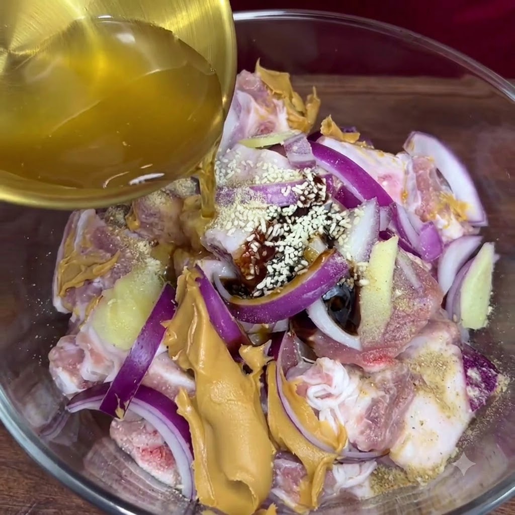 Jugo de ajo dorado siendo vertido desde un cucharón hacia el tazón de vidrio que contiene las costillas de cerdo sazonadas y otros ingredientes del adobo.