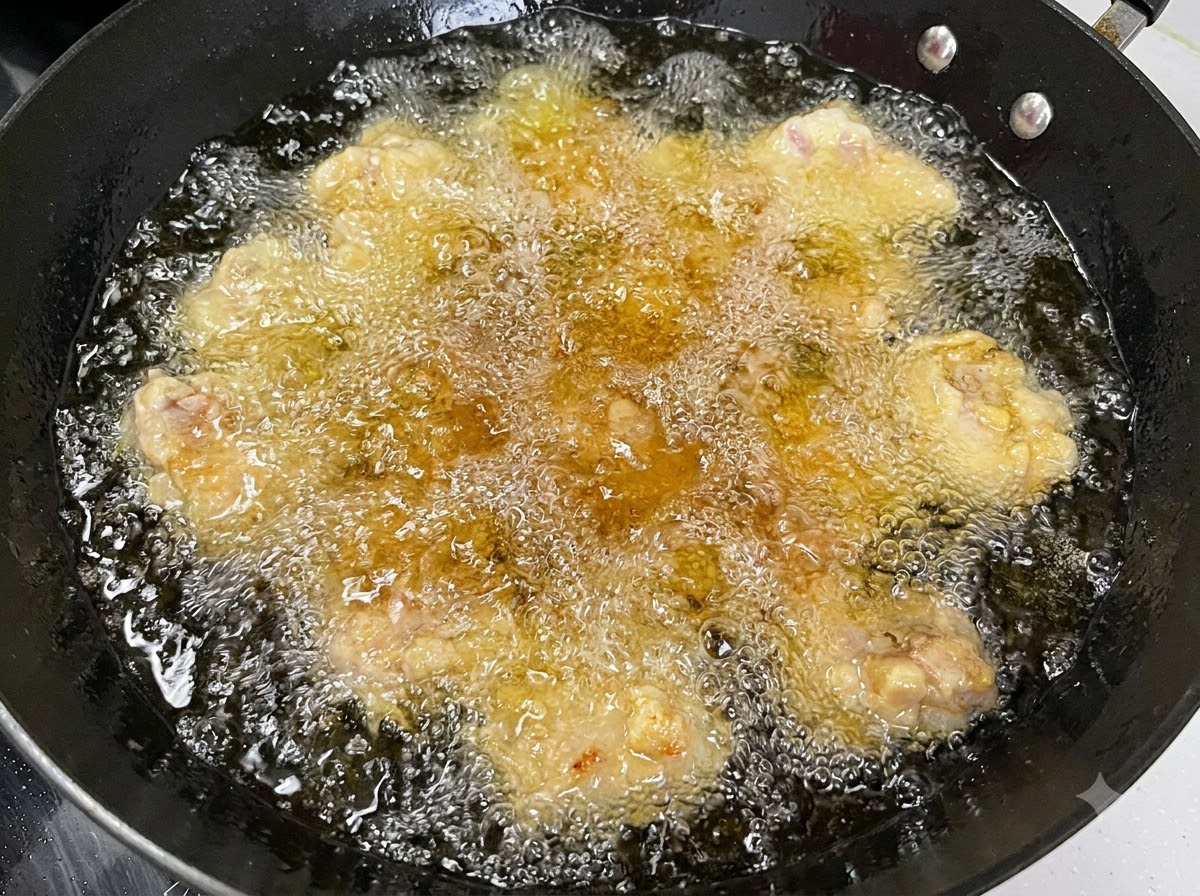 Múltiples trozos de costilla de cerdo friéndose en aceite caliente y burbujeante dentro de un wok negro.
