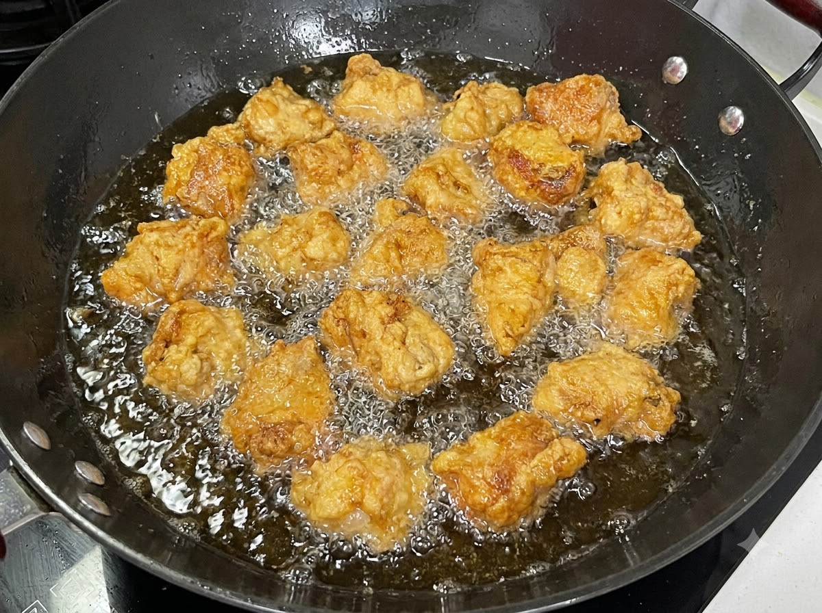 Trozos de costillas de cerdo rebozadas friéndose en un wok negro lleno de aceite burbujeante.